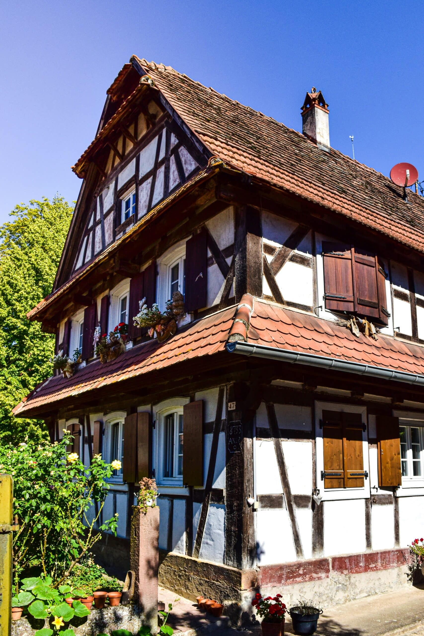 Maison traditionnelle alsacienne à colombages avec volets en bois et fleurs, ciel bleu en fond